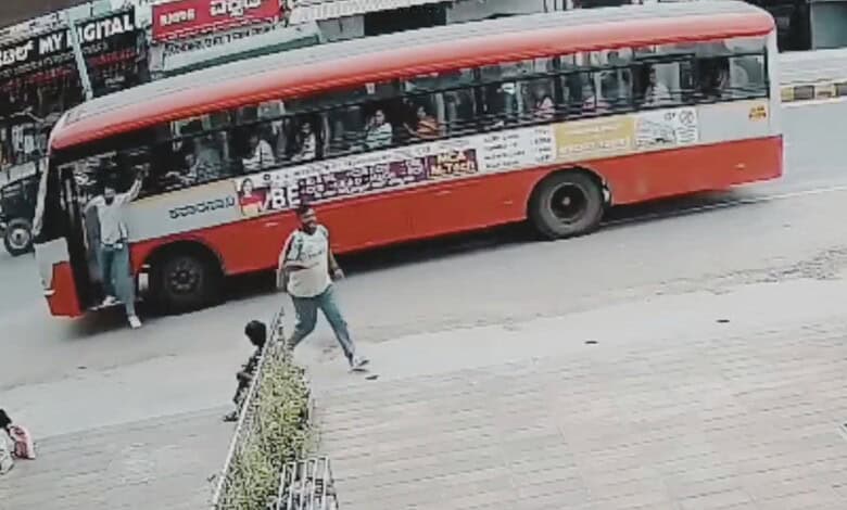A red and white KSRTC bus on the road with passengers and a person walking nearby.