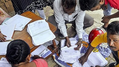 Voters' list verification process with officials and volunteers handling documents outdoors.