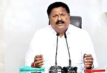 Ex-AP minister speaking at a press conference with microphones and documents on the table.
