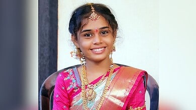 Smiling young girl in traditional pink saree with gold jewellery and bindi.