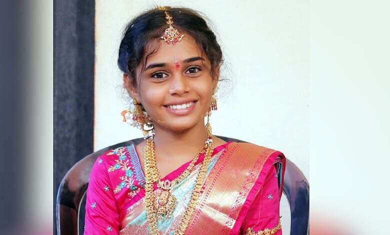 Smiling young girl in traditional pink saree with gold jewellery and bindi.