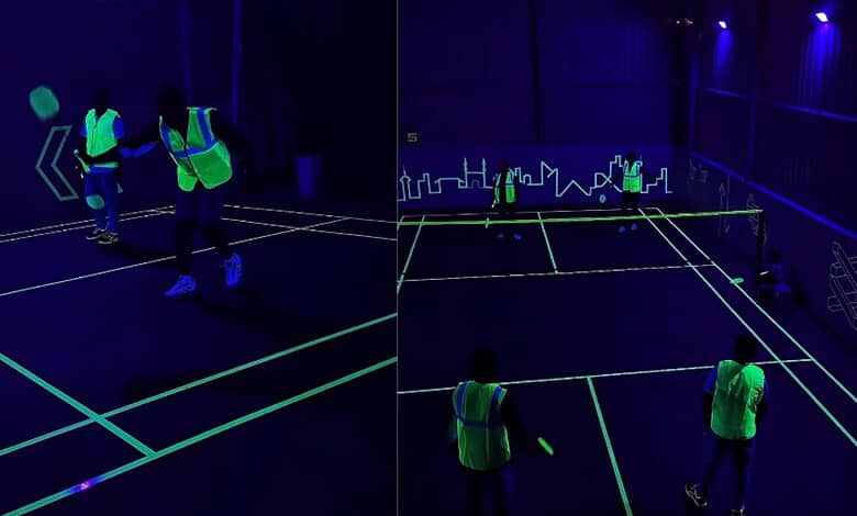 People playing badminton on a neon-lit dark court in Hyderabad.