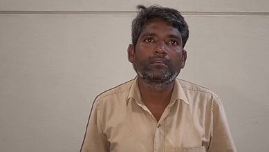 Man with a serious expression in beige shirt against plain wall background.