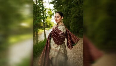 Elegant woman in traditional attire walking in lush green park during daytime.