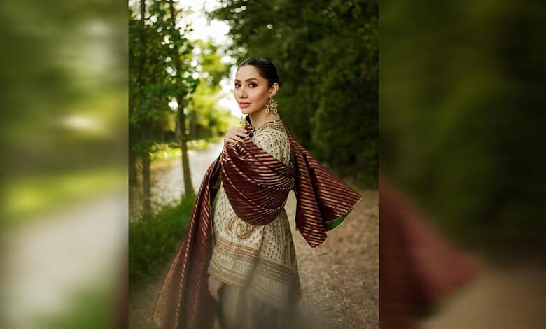 Elegant woman in traditional attire walking in lush green park during daytime.