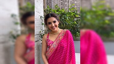Malavika Sharma smiling in a pink saree with gold embroidery, outdoors with greenery in the background.