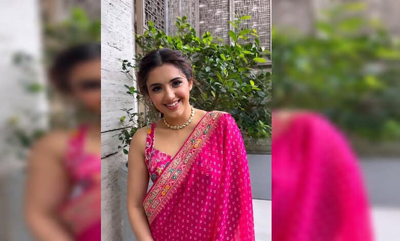 Malavika Sharma smiling in a pink saree with gold embroidery, outdoors with greenery in the background.