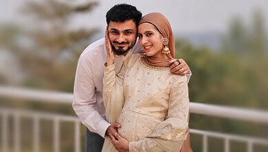 Joyful couple with a newborn, celebrating their first child, outdoors with a blurred background.