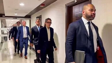 Group of professionals walking in a corridor, dressed in formal business attire.