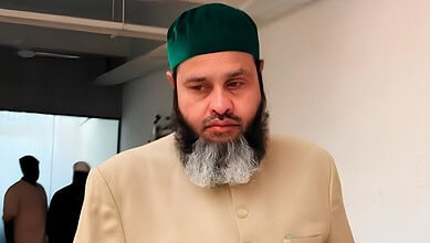 Close-up of a man with a beard wearing a green cap and beige traditional attire.