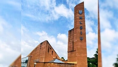 NLSIU campus building with blue sky and clouds, featuring the university's name on a tall tower.