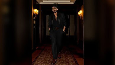 Nagarjuna in black suit walking confidently in a luxurious corridor.