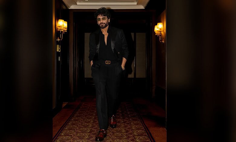 Nagarjuna in black suit walking confidently in a luxurious corridor.