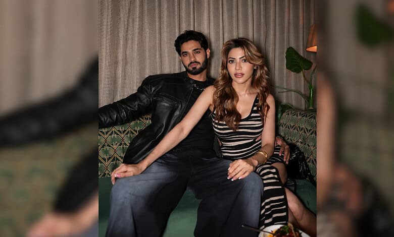 Nikki Tamboli sitting with a man in a cozy indoor setting, both looking at the camera.