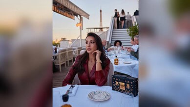 Nora Fatehi seated at a rooftop restaurant during sunset, with a city skyline in the background.