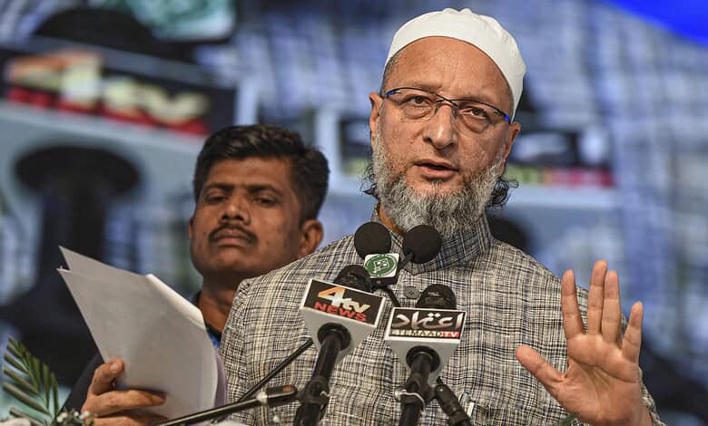 Asaduddin Owaisi speaking at a rally with microphones and supporters in the background.