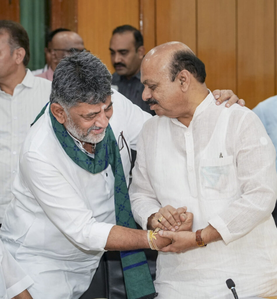 Karnataka leaders Shivakumar and another politician in a warm handshake at a political meeting.