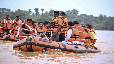 Rescue team in orange life jackets evacuates people by boat during Odisha flood.