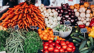 Fresh vegetables including carrots, onions, tomatoes, cucumbers, and peppers at a market stall.