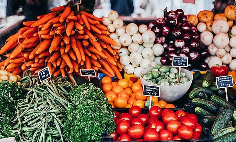 Fresh vegetables including carrots, onions, tomatoes, cucumbers, and peppers at a market stall.
