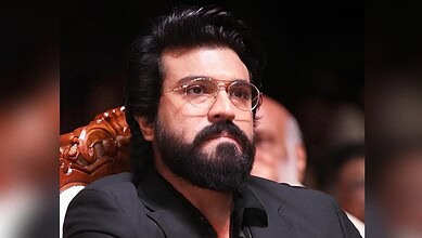 Ram Charan with a serious expression, wearing glasses and a black suit.