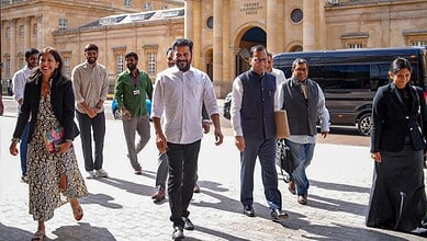 Group of politicians walking outside historic building in daylight, smiling and engaged.