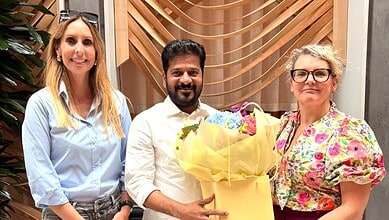 Group of three professionals smiling, holding a bouquet of flowers, in a modern office setting.