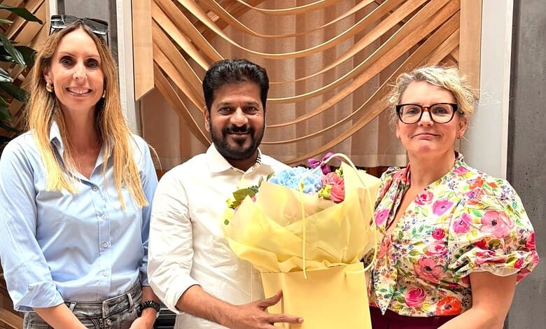 Group of three professionals smiling, holding a bouquet of flowers, in a modern office setting.