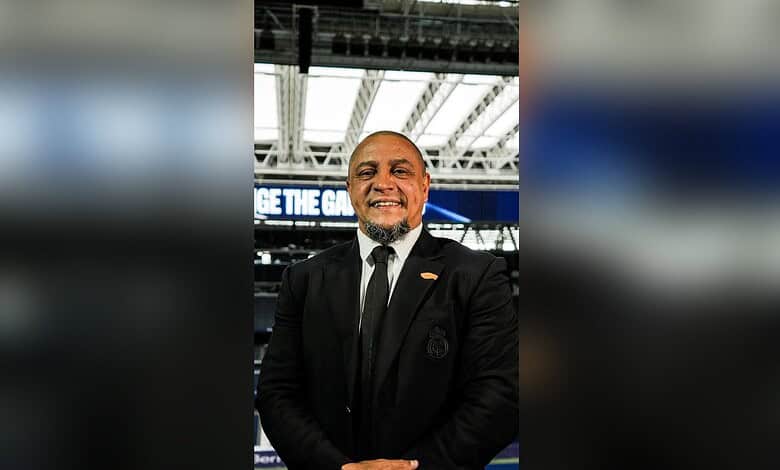 Roberto Carlos smiling at a Moroccan wedding, wearing a black suit and tie.