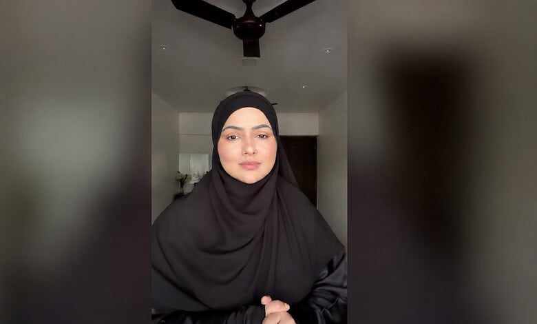 Sana Khan wearing a black hijab and looking at the camera in a modern indoor setting.