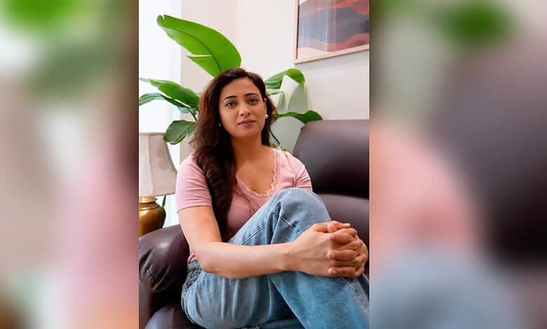 Shweta Tiwari seated on a sofa during an interview, wearing a pink top and blue jeans.