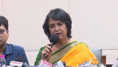 Taslima Nasreen speaking at a press conference with microphones in front of her.