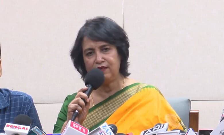 Taslima Nasreen speaking at a press conference with microphones in front of her.