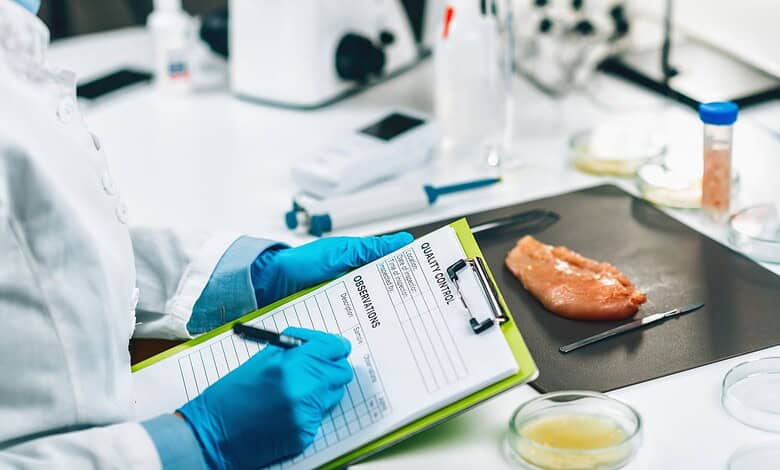 Food testing laboratory with a scientist recording results and chicken sample on a black tray.