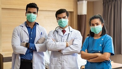 Group of three medical professionals wearing masks in a hospital room.