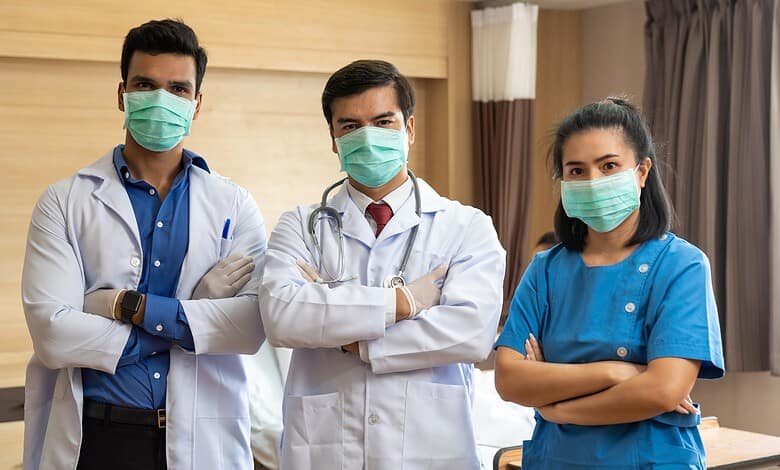 Group of three medical professionals wearing masks in a hospital room.