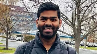 Smiling man with black hair and beard wearing a black jacket outdoors in winter.