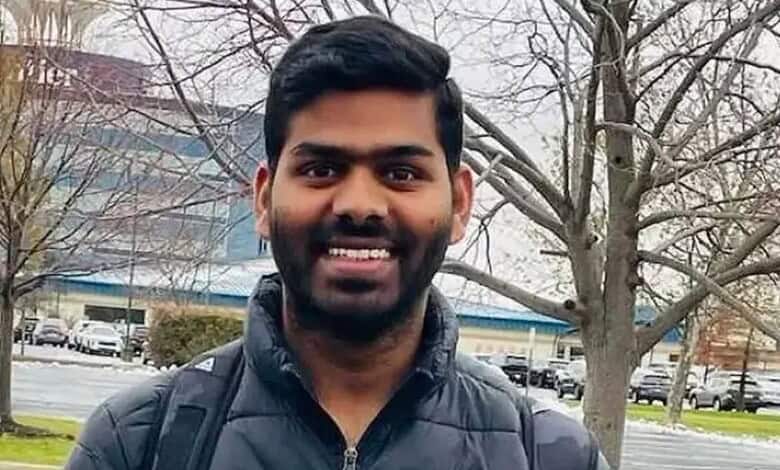 Smiling man with black hair and beard wearing a black jacket outdoors in winter.