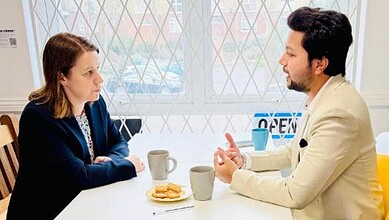 Two individuals engaged in a serious conversation at a table with coffee cups and snacks.