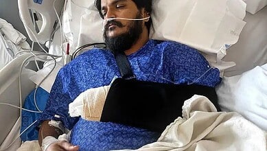 Injured man lying in hospital bed with arm in a sling and medical equipment nearby.
