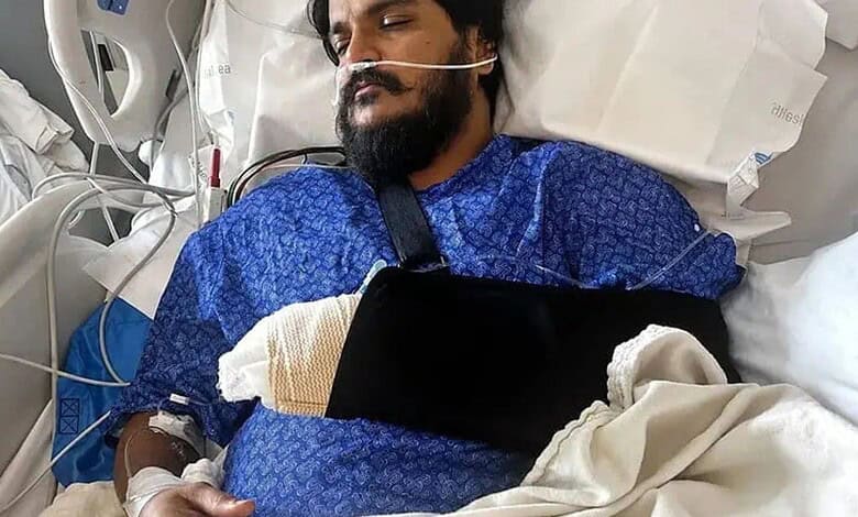 Injured man lying in hospital bed with arm in a sling and medical equipment nearby.
