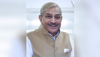 Smiling elderly man with grey hair and beige vest in an indoor setting.