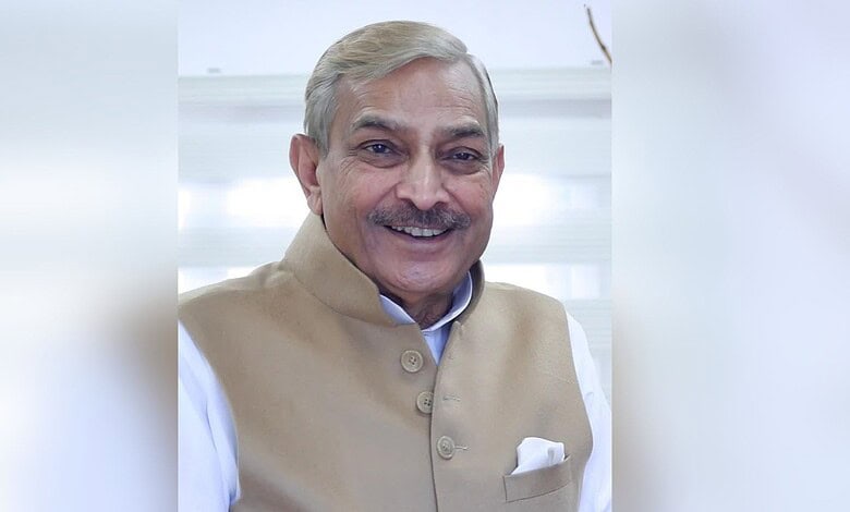 Smiling elderly man with grey hair and beige vest in an indoor setting.