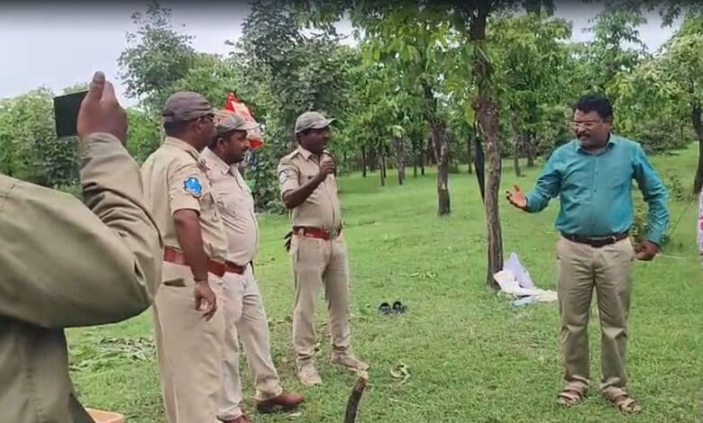 Man in blue shirt speaking to police officers in a park with trees and grass.