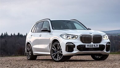 White BMW X7 SUV parked outdoors with a scenic background of trees and sky.