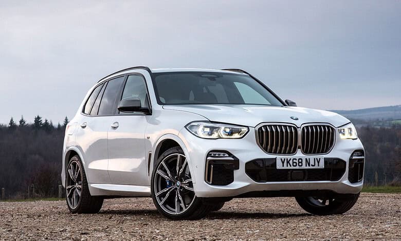 White BMW X7 SUV parked outdoors with a scenic background of trees and sky.