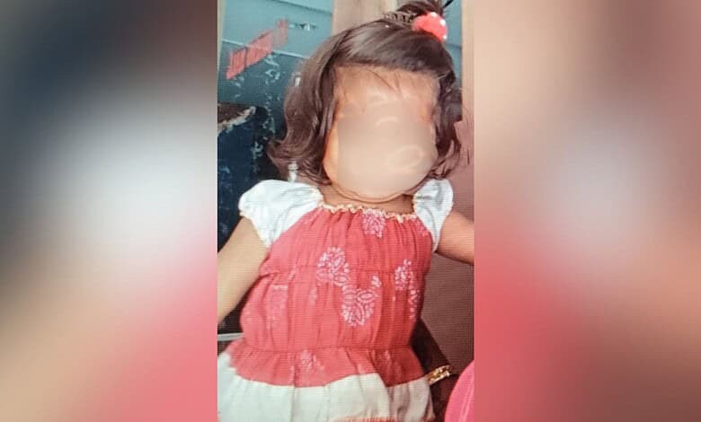 Child with blurred face wearing a red and white dress, sitting indoors.