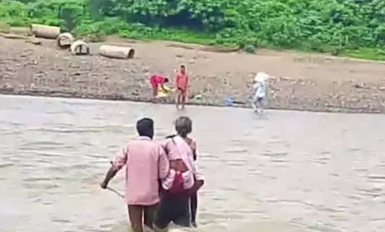 Man carries mother through flooded stream in Asifabad district