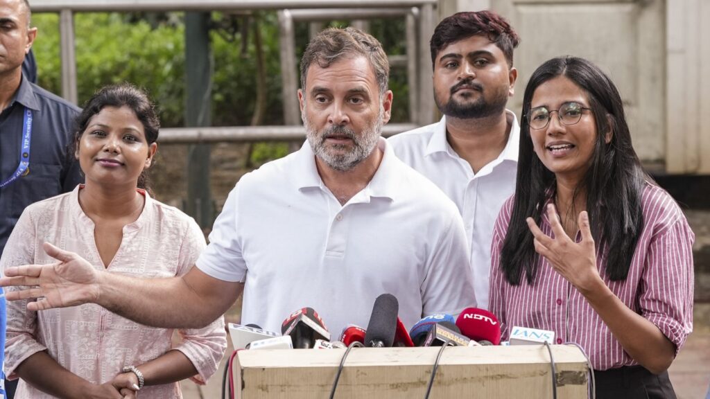 Rahul Gandhi speaking at a press conference with women supporters in the background.