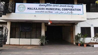Entrance of Malkajgiri Municipal Corporation building with signage in multiple languages.